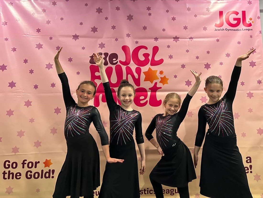 Four gymnasts posing in front of the JGL Fun Meet backdrop